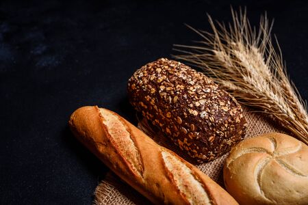 Fresh fragrant bread with grains and cones of wheat against a dark background