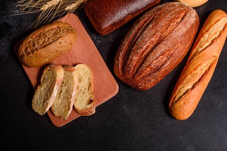 Fresh fragrant bread with grains and cones of wheat against a dark background. Assortment of baked bread on wooden table background. Fresh fragrant bread on the table. Food concept.の写真素材