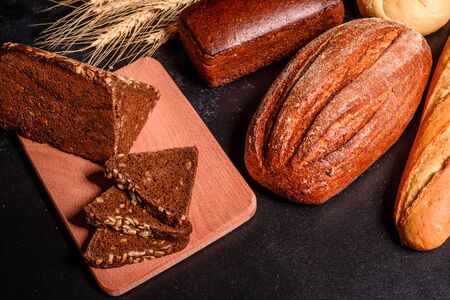Fresh fragrant bread with grains and cones of wheat against a dark background. Assortment of baked...