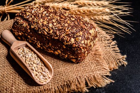 Fresh fragrant bread with grains and cones of wheat against a dark background. Assortment of baked...