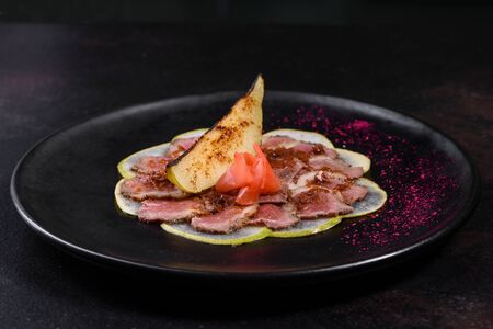 Edged pieces with caramelized pear on a black ceramic plate. Baked meat sliced with thin piecesの写真素材