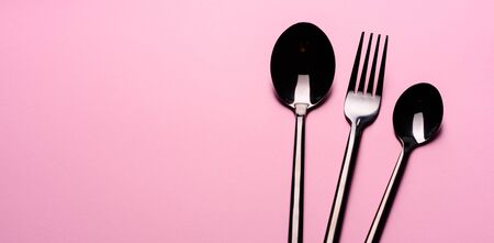 Metal Spoon and fork Isolated on pink background. Set of tableware ready for the meal with pink copy...