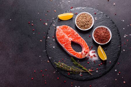 Raw trout red fish steak served with herbs and lemon and olive oil on a dark background. Cooking Salmon, sea food. Healthy eating conceptの写真素材