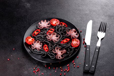 Black seafood pasta with shrimp, octopus and mussels on black background. Mediterranean gourmet food. Black pasta with octopus on a black stone plateの写真素材