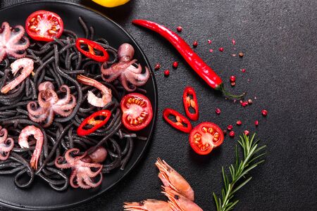 Black seafood pasta with shrimp, octopus and mussels on black background. Mediterranean gourmet food. Black pasta with octopus on a black stone plateの写真素材