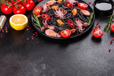 Black seafood pasta with shrimp, octopus and mussels on black background. Mediterranean gourmet food. Black pasta with octopus on a black stone plateの写真素材