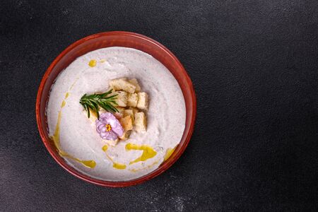Delicious beautiful mushroom soup in a brown plate with a wooden spoon on a dark brown backgroundの写真素材