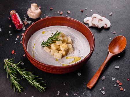 Delicious beautiful mushroom soup in a brown plate with a wooden spoon on a dark brown backgroundの写真素材