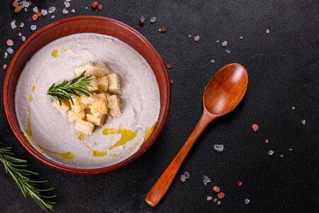 Delicious beautiful mushroom soup in a brown plate with a wooden spoon on a dark brown backgroundの写真素材