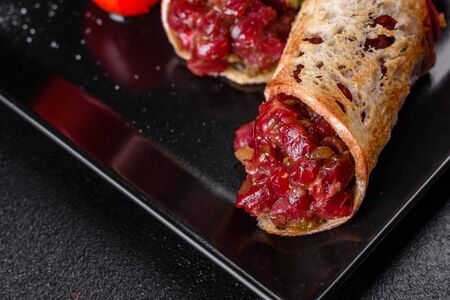Delicious fresh beef tartar with toasts on a black square plate against a dark backgroundの写真素材