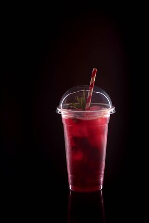 Refreshing cool lemonade with strawberries, mint and ice in plastic glass with lid on black backgroundの写真素材