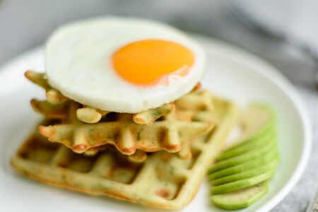 Fresh delicious and nutritious breakfast with waffles with spinach, fried egg and avocado piecesの写真素材