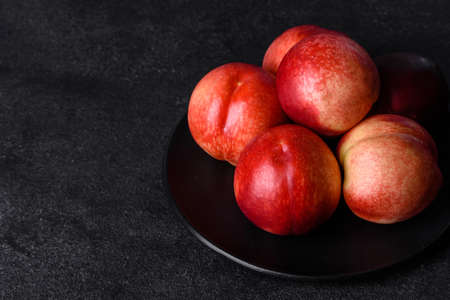 Delicious sweet peaches or nectarines in a brown bowl on a dark concrete backgroundの写真素材