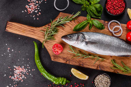 Fresh fish seabass and ingredients for cooking. Raw fish seabass with spices and herbs on a dark tableの写真素材