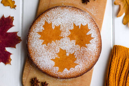 Beautiful fresh sweet pumpkin cake with a maple leaf pattern on a white wooden background with a...