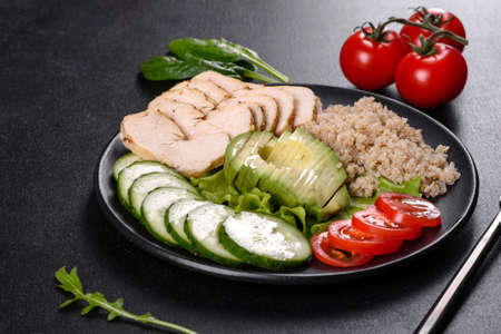 Fresh delicious salad with quinoa, chicken and fresh vegetables on a plate on a dark concrete...