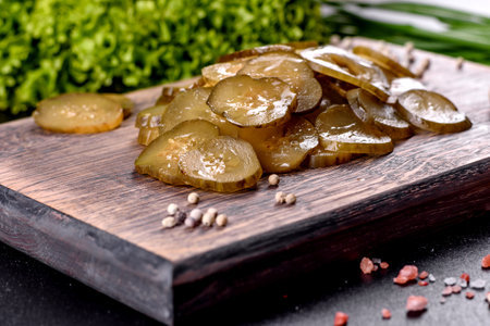 Tasty salty spicy pickled cucumber cut with rings on a wooden cutting board on a dark concrete backgroundの写真素材