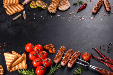 Tasty, fresh sausages grilled with vegetables spices and herbs. Photo of the finished dish on a dark...