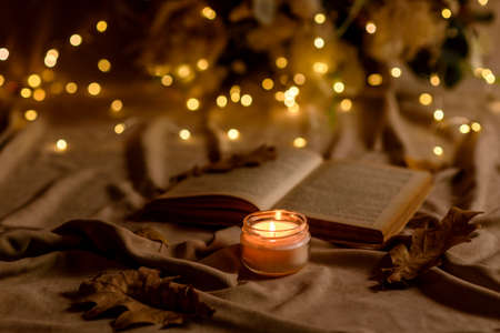 A burning candle on a wooden table in front of a book in a half-mast. Learning. Studying the Bible