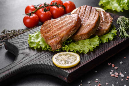 Delicious juicy tuna steak grilled with spices and herbs and lemon slices on a dark backgroundの写真素材