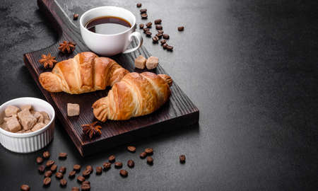 Fresh crisp delicious French croissant with a cup of fragrant coffee on a dark concrete background....
