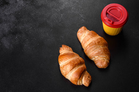 Fresh crisp delicious French croissant with a cup of fragrant coffee on a dark concrete background. Invigorating breakfastの写真素材