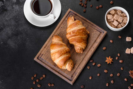 Fresh crisp delicious French croissant with a cup of fragrant coffee on a dark concrete background. Invigorating breakfastの写真素材