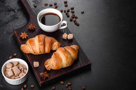 Fresh crisp delicious French croissant with a cup of fragrant coffee on a dark concrete background. Invigorating breakfastの写真素材
