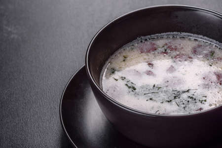 Cheese soup with fried sausages and herbs. Tasty cream cheese soup in a black plate. Dinner tableの写真素材