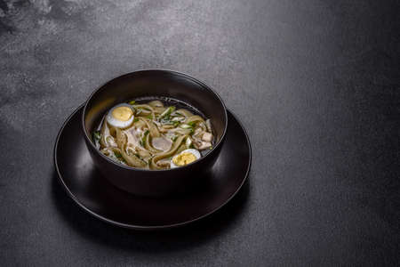 Fresh delicious hot soup with noodles and quail egg in a black plate on a dark backgroundの写真素材
