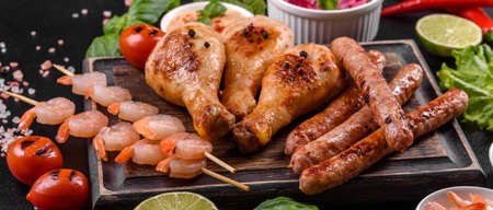 Composition of sausages, chicken, pork and shrimp prepared on grill, as well as vegetables prepared...