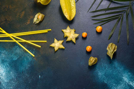 Fruit carambol, beach accessories and foliage of a tropical plant on colored paper. Summer...