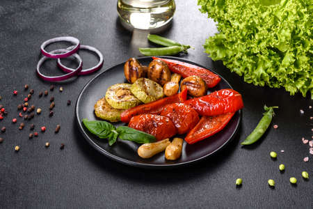 Tasty fresh vegetables grill: tomatoes, peppers, mushrooms, zucchini and onions on a black plate. Delicious healthy foodの写真素材
