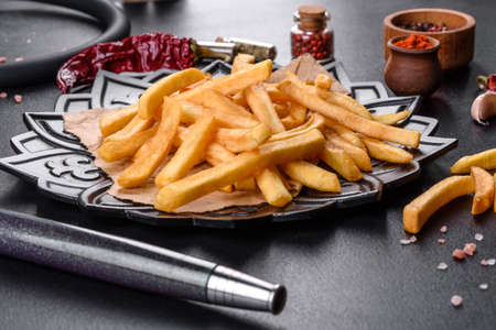 Tasty fried french fries with salt and spices on a dark background. Unhealthy food