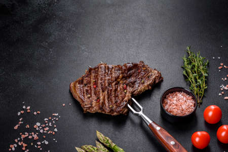 Delicious juicy fresh beef steak with spices and herbs on a dark concrete background. Grilled dishesの写真素材