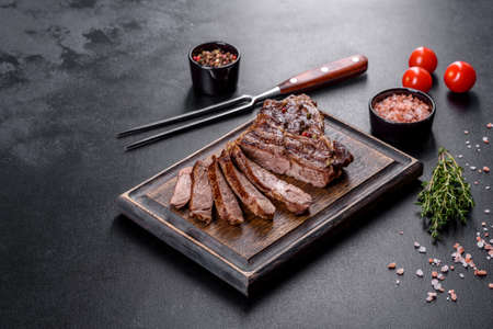 Delicious juicy fresh beef steak with spices and herbs on a dark concrete background. Grilled dishesの写真素材