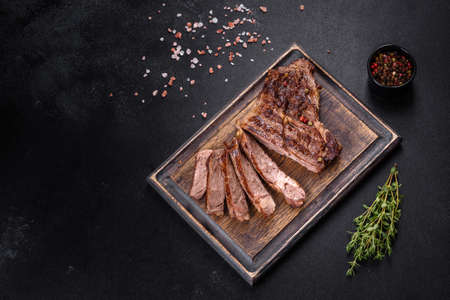 Delicious juicy fresh beef steak with spices and herbs on a dark concrete background. Grilled dishes