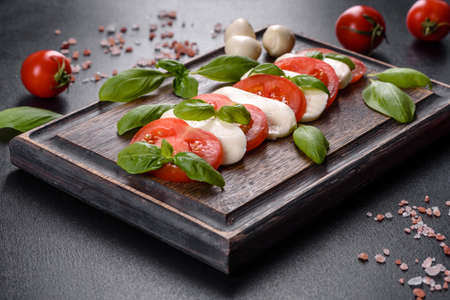 Italian caprese salad with sliced tomatoes, mozzarella cheese, basil, olive oil. Served in vintage black plate on a dark concrete backgroundの写真素材