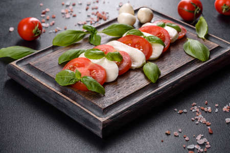 Italian caprese salad with sliced tomatoes, mozzarella cheese, basil, olive oil. Served in vintage black plate on a dark concrete backgroundの写真素材