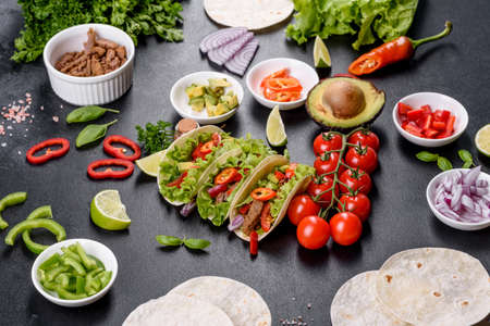 Mexican tacos with beef, tomatoes, avocado, onion and salsa sauce on a dark concrete backgroundの写真素材