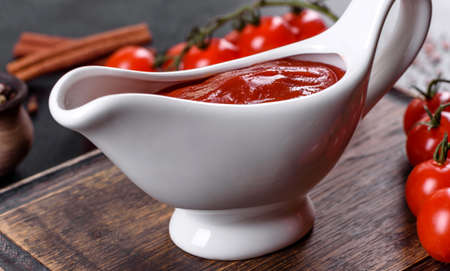 Red sauce or ketchup in a bowl and ingredients for cooking, spices, garlic, tomatoes and herbs on a black backgroundの写真素材