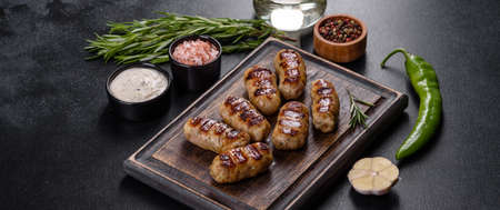 Grilled sausage with the addition of herbs and vegetables on the dark background. Grilling food,...