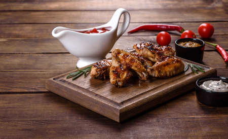 Grilled spicy chicken wings on a dark background with spices and herbs. Unhealthy food cooked on fireの写真素材