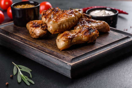 Grilled spicy chicken wings on a dark background with spices and herbs. Unhealthy food cooked on...