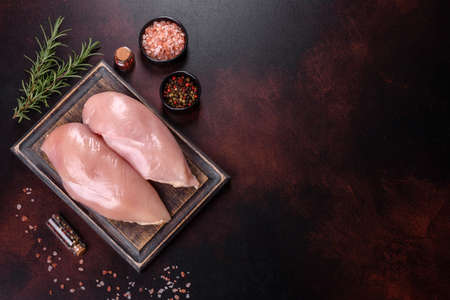 Raw chicken fillet on a cutting board with spices on a dark background. Top viewの写真素材