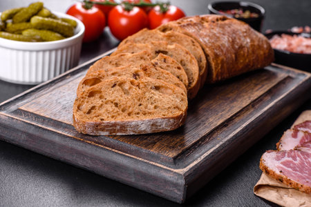Delicious fresh bacon sliced with bread and vegetables on a dark concrete background