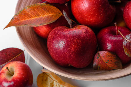 Beautiful fresh red apples with autumn leaves in a wooden vase on a light concrete table. Harvest seasonの写真素材
