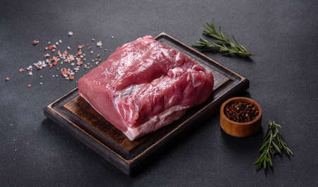 Raw pork steak on a cutting board with herbs and spices on dark stone tableの写真素材