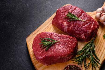 Raw beef steaks on a cutting board with spices on a stone backgroundの写真素材