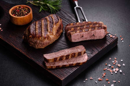 Fresh juicy delicious beef steak on a dark background. Meat dish with spices and herbsの写真素材